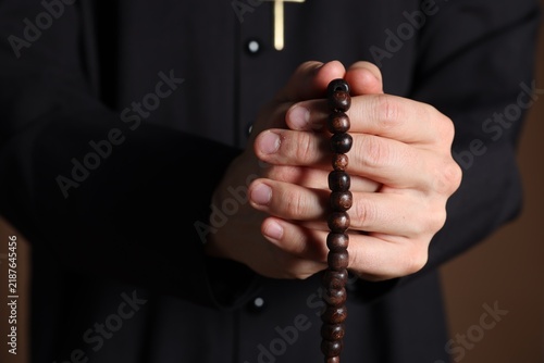 Canvas Print Priest in cassock with rosary on brown background, closeup