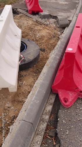 Concrete curb being installed along an excavated sidewalk during urban improvement works, with temporary safety barriers surrounding the work area