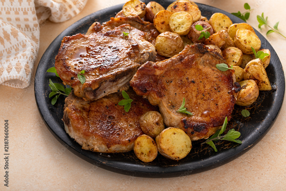 Obraz premium Pork chops on a bone grilled or sauteed served with roasted potatoes on a plate