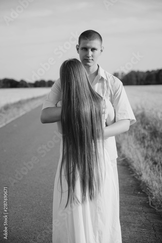 Bild auf Leinwand Young couple embracing on a rural road surrounded by fields, seen from behind