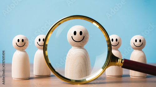 Magnifying glass focusing on a happy wooden person figure among others with smiley faces image