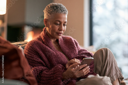 Older woman using smartphone while relaxing in cozy living room  