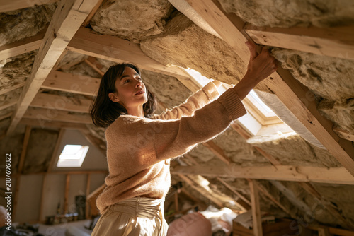 Young woman renovating attic by installing wooden beams in cozy space  