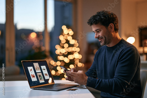 Man using smartphone while working on laptop at home during holidays  