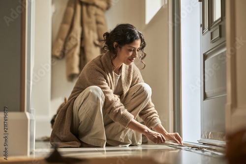 Young woman sitting on the floor adjusting a door mat in a hallway  