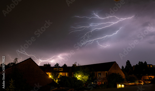 Dramatic spider lightning over residential neighborhood at night illuminating clouds and houses.