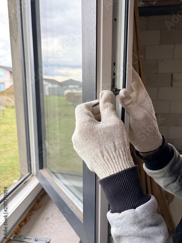 A worker adjusts the mechanism of a modern window frame. Manual window frame adjustment