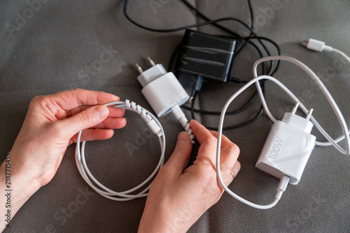 Hands holding a charging cable while connecting it to various power adapters on a table