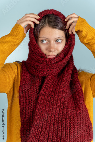 Woman wearing a red scarf with an orange sweater against a light blue background