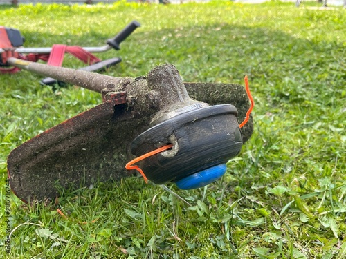 Grass trimming tool rests on green grass in a garden during daylight hours