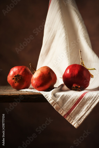 Pomegranate Still Life.  Three ripe pomegranates on shelf with kitchen towel.