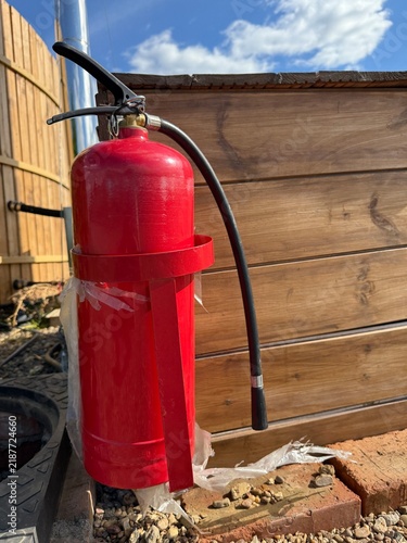 Red fire extinguisher mounted on wooden wall in outdoor setting