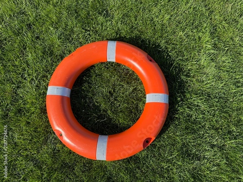 Orange life buoy on green grass background, safety equipment for water