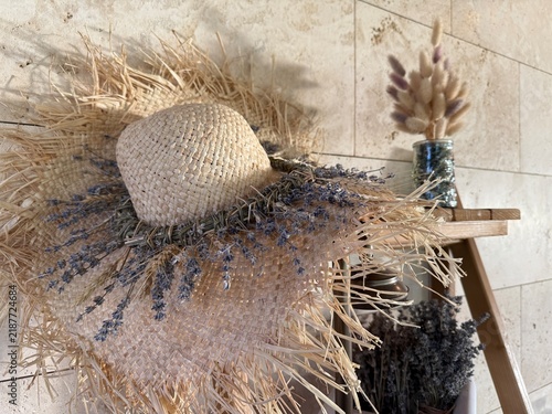 Straw hat decorated with dried lavender on wooden shelf in rustic setting
