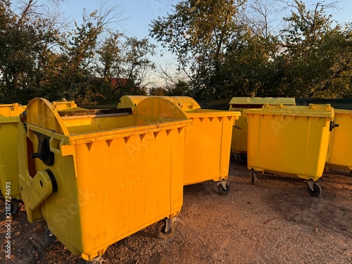 Yellow waste containers lined up in outdoor recycling area during sunset