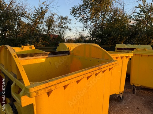 Yellow waste containers in outdoor setting with trees and clear sky