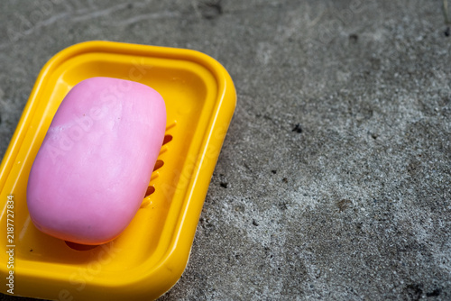 Fotografía Pink soap bar placed on a yellow soap dish resting on a textured gray surface, s