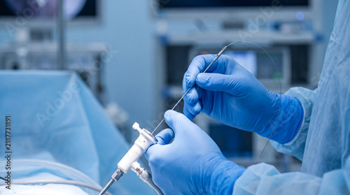 Surgeon hands in blue gloves operating a laparoscopic micro-grasper instrument in a sterile hospital