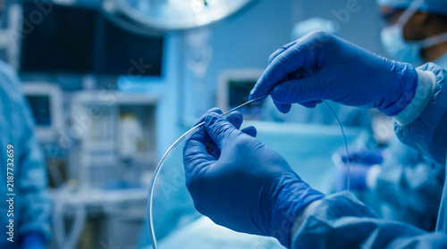 Surgeon hands in blue gloves performing a medical procedure with a catheter in a sterile operating room