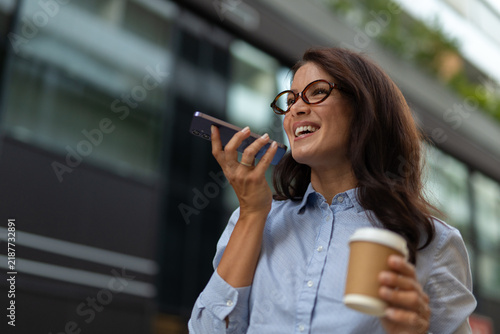 Foto Businesswoman talking on speakerphone holding coffee in city