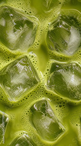 Top view of iced matcha latte in short glass with five large ice cubes submerged in pale creamy green liquid, placed on dark wooden slatted table Stock Photo