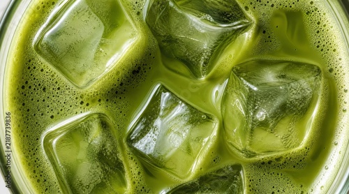Top view of iced matcha latte in short glass with five large ice cubes submerged in pale creamy green liquid, placed on dark wooden slatted table Stock Photo