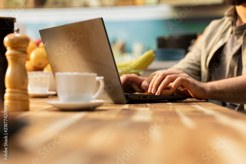 Canvastavla Man works from home on a laptop at a kitchen table, combining online tasks and digital multitasking with a casual remote-worker routine in natural light