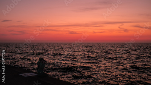 Girl taking pictures next to the sea at sunrise