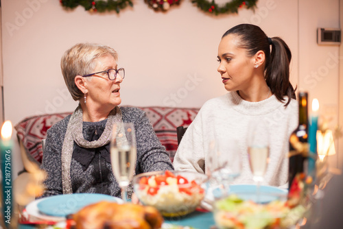 Canvas Print Older and younger women talk face to face at a festive dinner table, conveying family connection, conversation and holiday togetherness at home