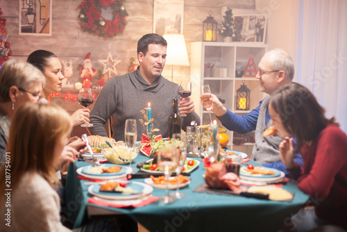 фотографія Adult and senior men raise wine glasses across a festive Christmas dinner table, sharing a celebratory moment of connection, togetherness and holiday cheer during a family toast at home