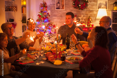 Obraz na plátně Smiling family members hold sparklers around a holiday feast, creating a lively Christmas celebration that highlights seasonal tradition, family bonding and togetherness in a warmly decorated home