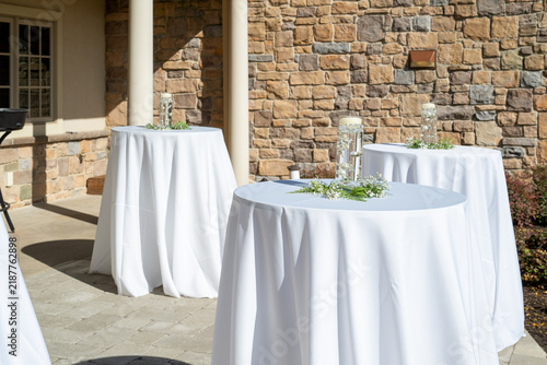 Foto Outdoor wedding reception cocktail tables with white tablecloths and greenery ce