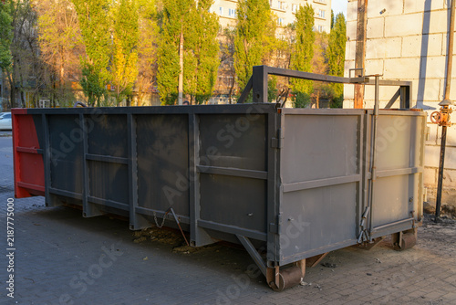 Heavy metal garbage container located in urban industrial area. Empty steel waste bin for construction debris and street cleanup. Real Photo