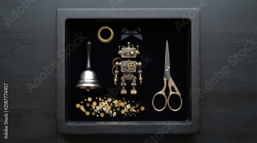 knolling arrangement of miniature robot, bell, ribbon scissors, and gold confetti on a dark presentation tray