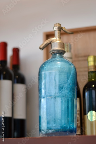 Obraz na plátně Antique Blue Glass Seltzer Siphon with Wine Bottles in Rustic Cellar Setting