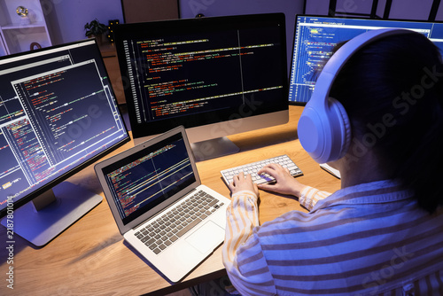 Female programmer with headphones working in office at night, back view