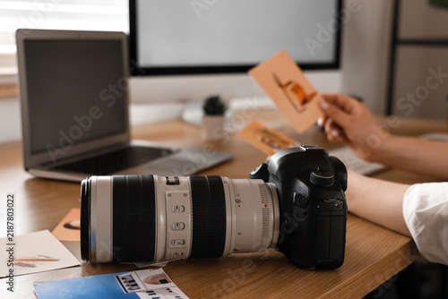 Camera on table against female photographer with pictures in office, closeup