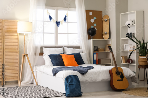 Interior of teenagers room with bed, lamp and shelf units