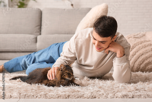 Young man with cute cat lying on carpet at home