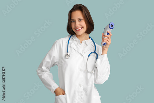 Beautiful female doctor with infrared thermometer on blue background