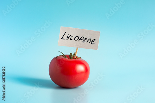 Fotografie A bright red tomato, close‑up, against a light background, with the word “lycopene” written on the paper label, also close‑up