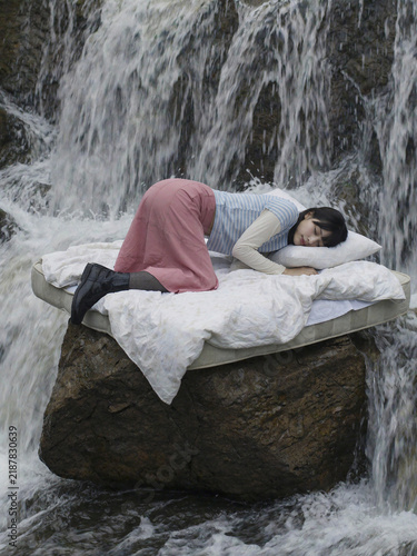 Obraz na płótnie 滝の上の岩に置かれたマットレスで眠る女性