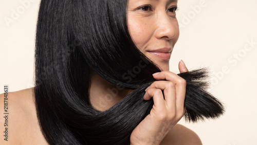 Woman holding a strand of her long straight black hair to showcase its healthy texture and shine during a close up beauty care product commercial shoot.