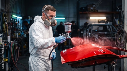Technician in protective suit spray painting red car part