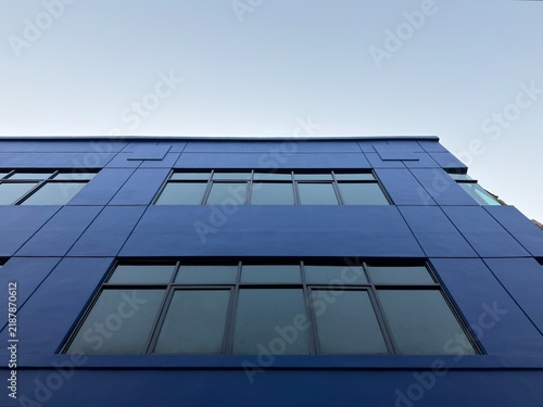 Modern blue building facade with glass windows under clear sky, low angle shot of urban architecture