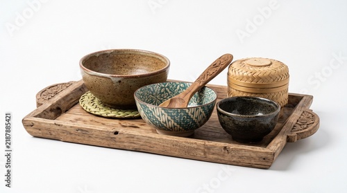 Tapety artystyczne Rustic ceramic bowls paired with ornate wooden spoon and bamboo container arranged neatly on decorative carved wooden serving tray isolated against clean white studio background