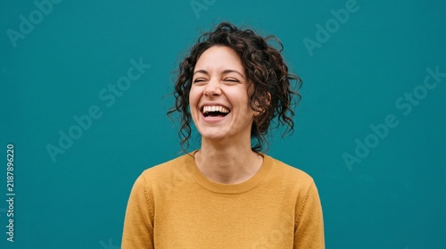 Portrait of a Joyful Young Woman Laughing Heartily Against a Solid Teal Background