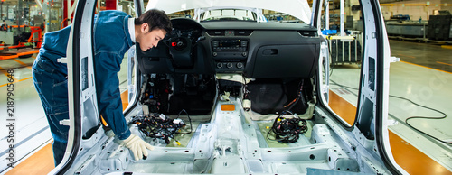 In the vehicle manufacturing workshop, industrial workers are installing wiring and interior components onto a body-in-white that has not yet undergone interior trim cladding.