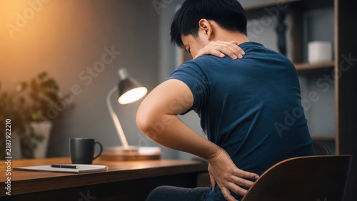 Young man sitting at desk holding neck and lower back, chronic office back pain concept