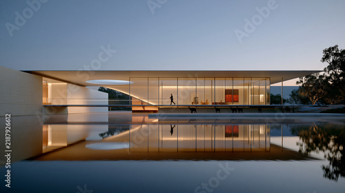 Minimalist glass house at dusk with warm interior glow and perfect water reflection. High quality photo